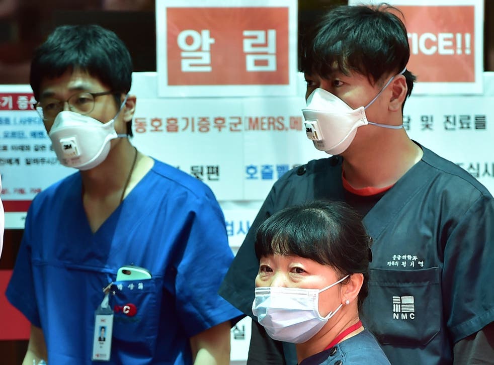 South Korean hospital workers wearing masks stand in front of a public notice on MERS while setting up a separated emergency center at the National Medical Center in Seoul
