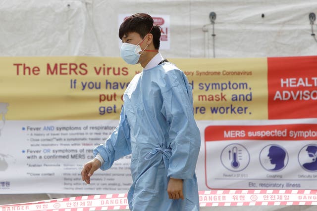 A hospital worker wearing mask walks in front of a health advisory sign at a quarantine tent for people who could be infected with the Mers virus at Seoul National University Hospital
