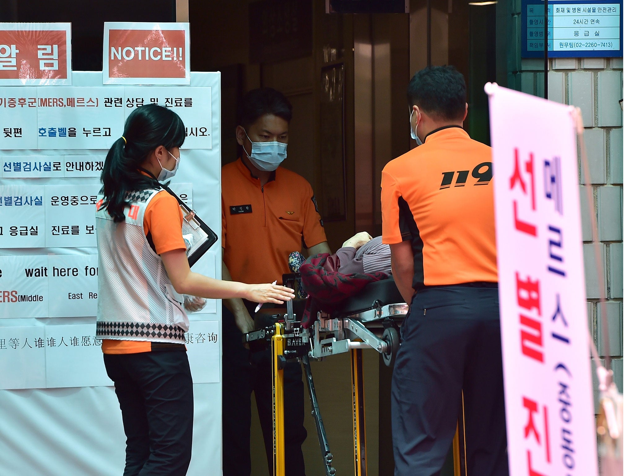 South Korean rescue members carry a woman in front of a public notice on MERS at the National Medical Center in Seoul