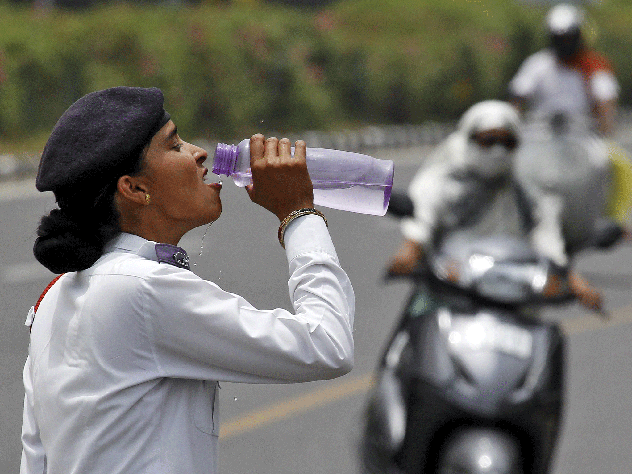 A traffic police woman drinks water as commuters drive along a road on a hot summer day in Chandigarh