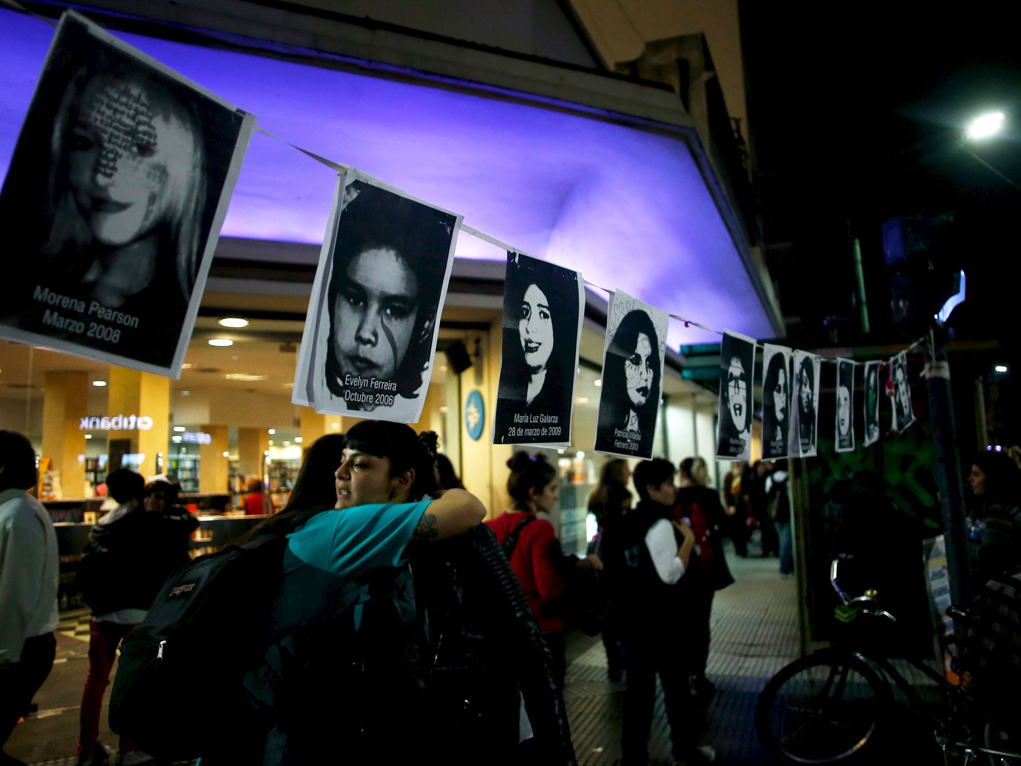 Two women embrace under pictures of victims of gender violence