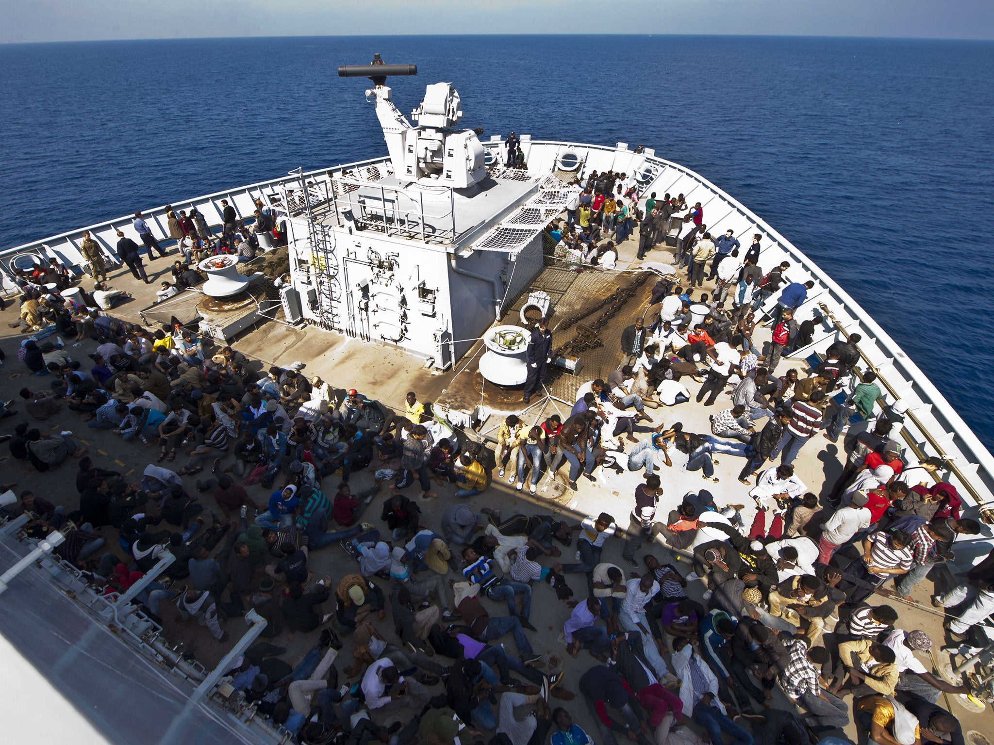 The rescued migrants sit on the deck of HMS ‘Bulwark’