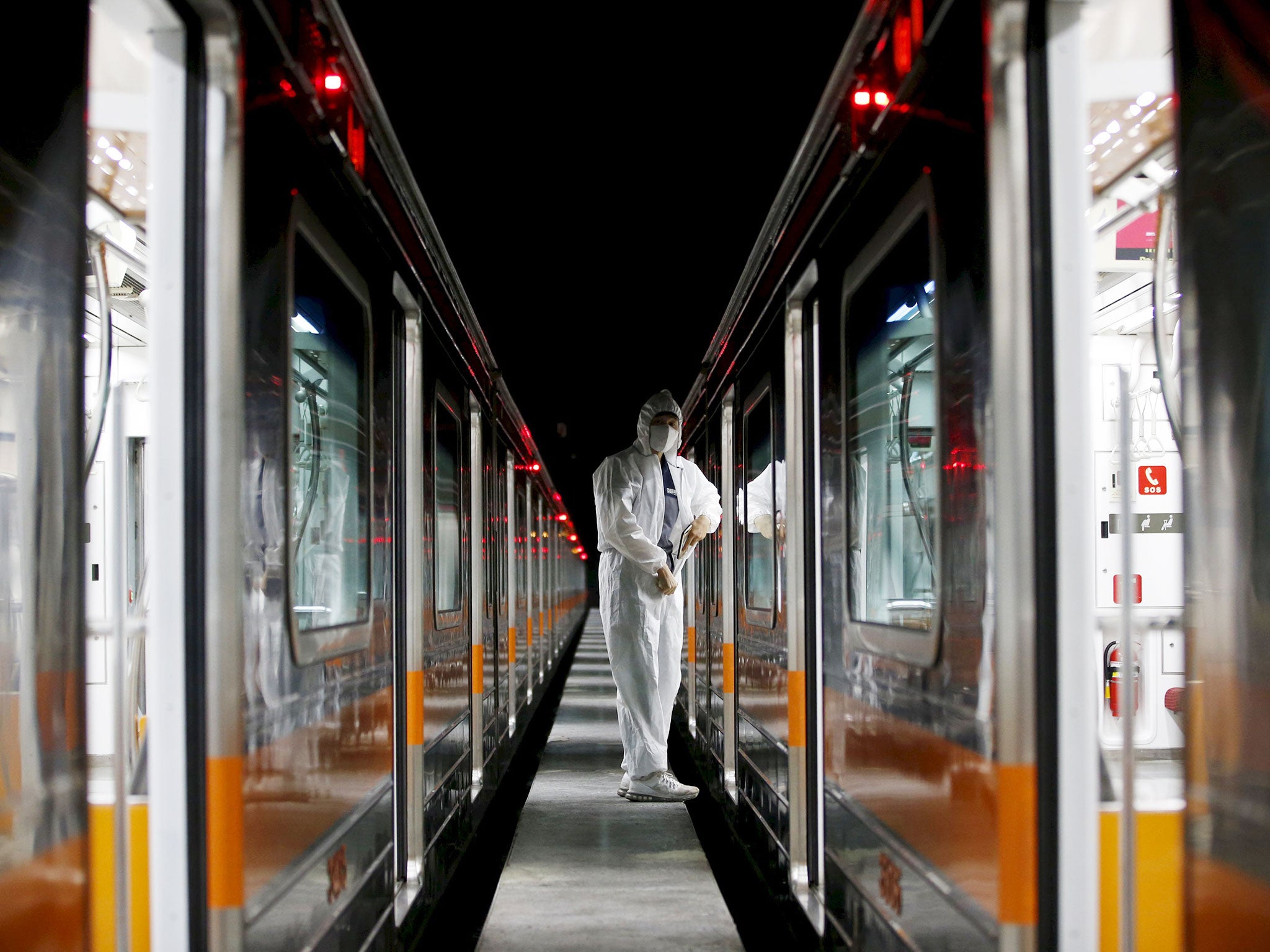 A worker in full protective gear adjusts his suit between subway trains on the Seoul Metro