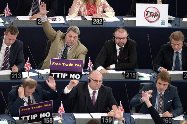 Members of the European Parliament take part in a voting session as they hold signs against TTIP