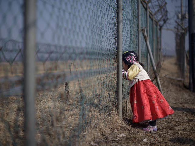 A girl stands at a military fence facing towards North Korea south of the Military Demarcation Line and Demilitarized Zone (DMZ) separating North and South Korea.