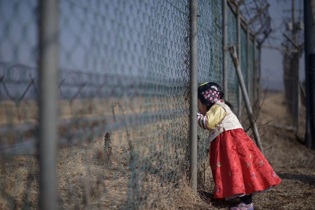 A girl stands at a military fence facing towards North Korea south of the Military Demarcation Line and Demilitarized Zone (DMZ) separating North and South Korea.
