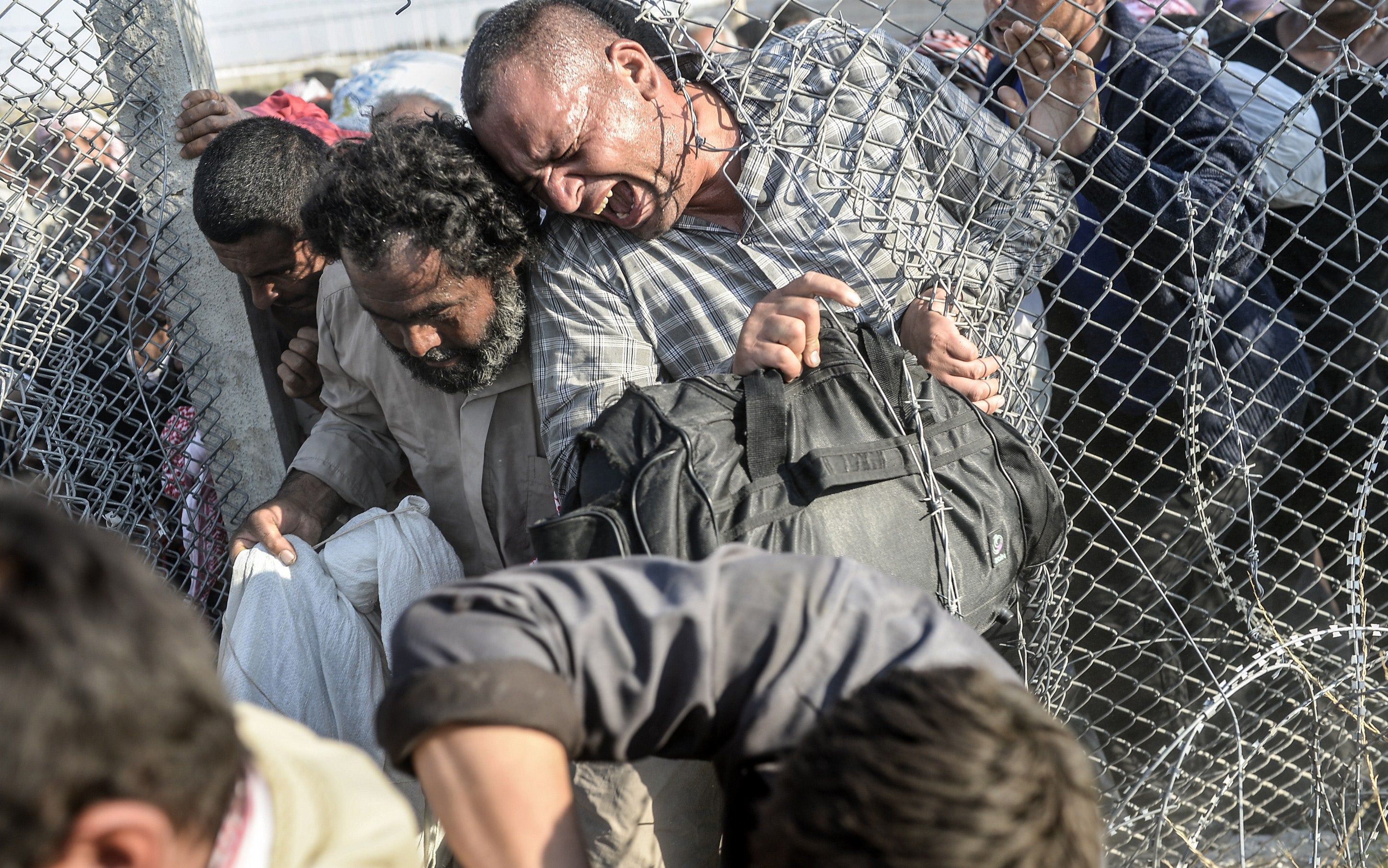 Men struggle through the wire fences (Photo: BULENT KILIC/AFP/Getty Images)