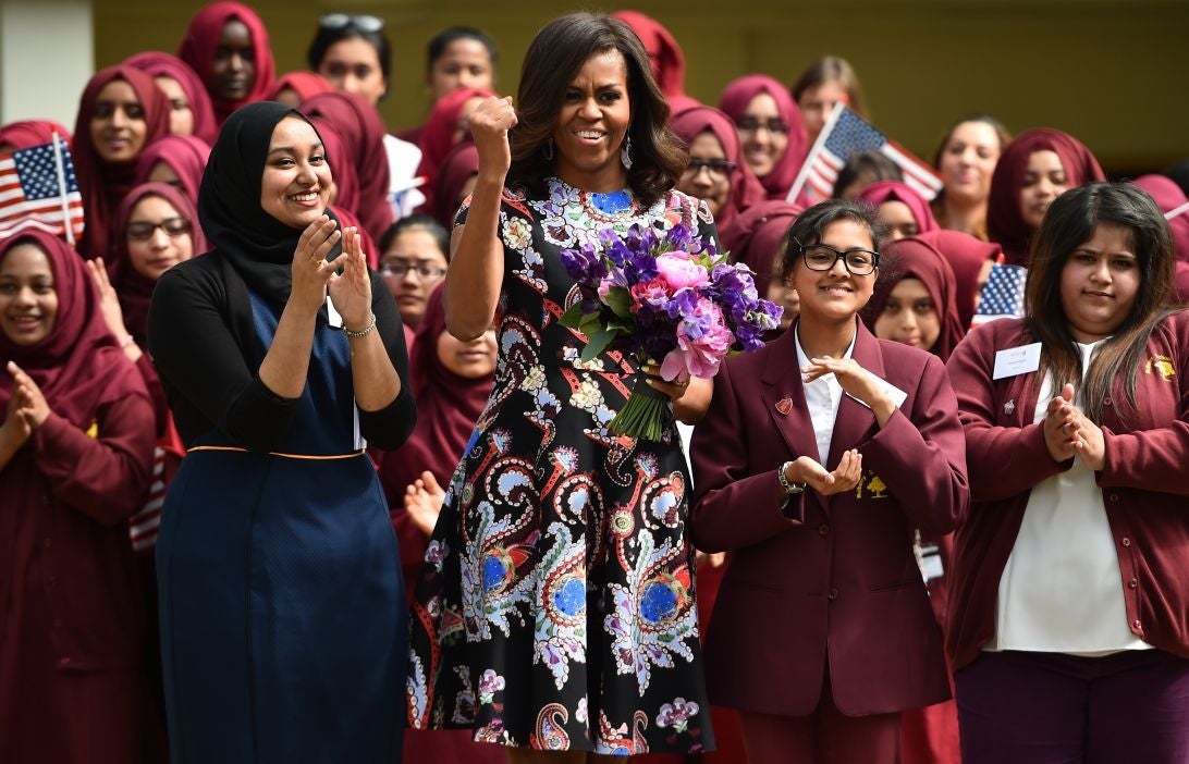 US First Lady Michelle Obama gestures and holds flowers as she is received by young students holding the American flag in the courtyard before an event as part of the 'Let Girls Learn Initiative' at the Mulberry School for Girls on June 16, 2015 in London