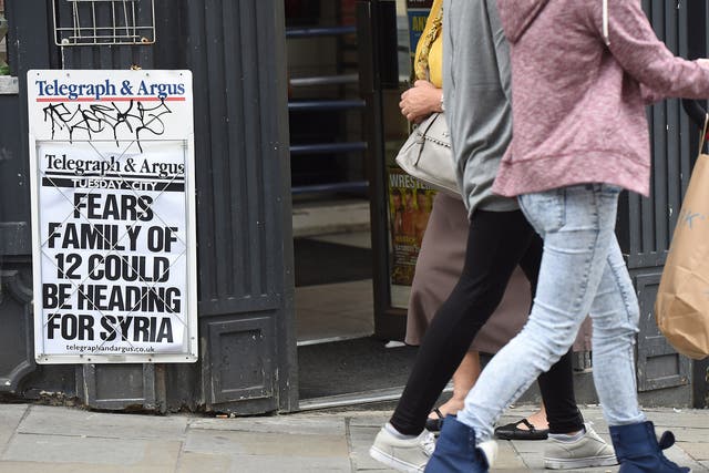 Pedestrians walk past a newsagents displaying a local paper headline on a notice board referring to fears regarding a missing family of 12 in Bradford