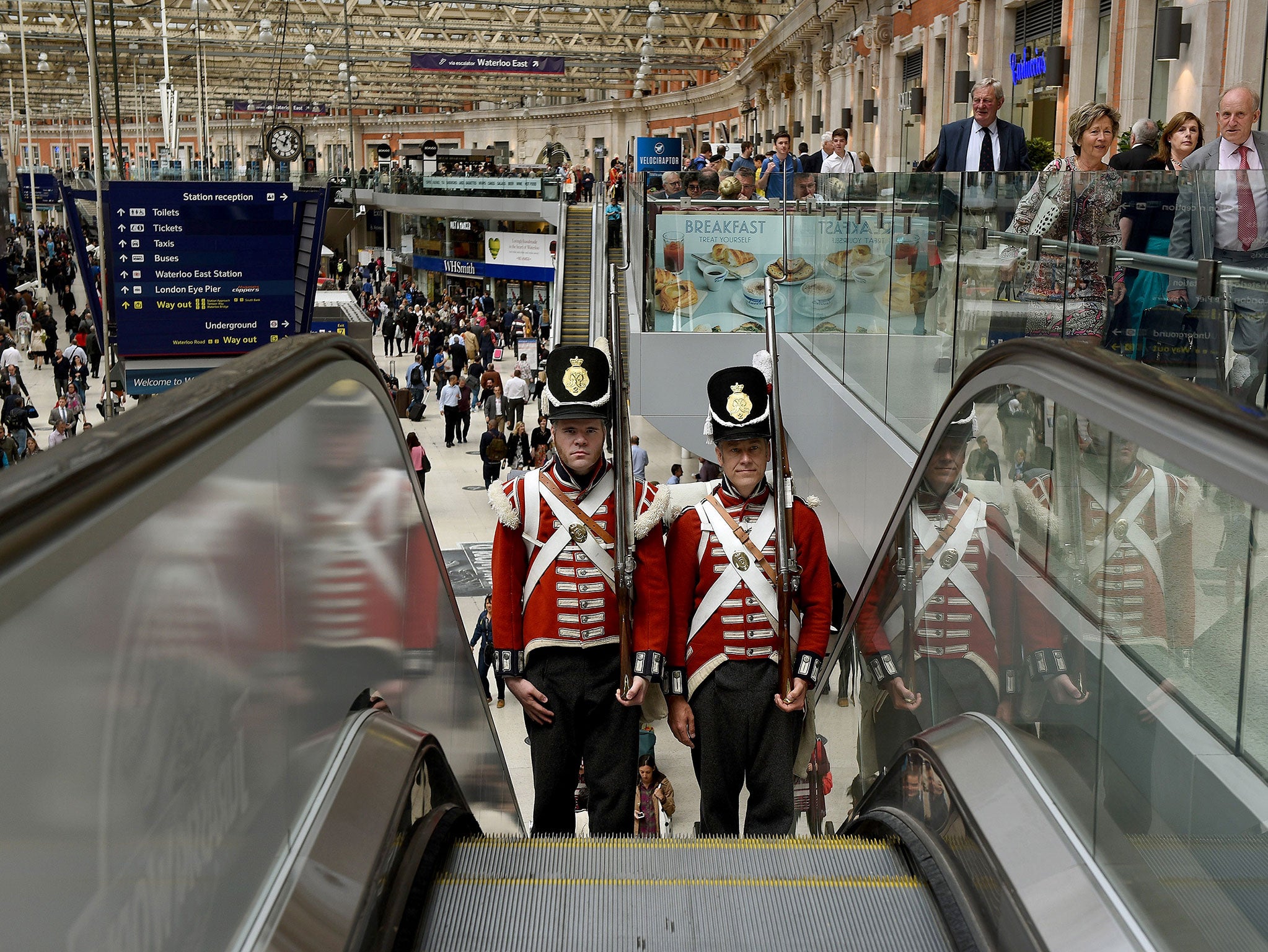 Men dressed as soldiers from the Grenadier Company during the Waterloo Campaign ride an escalator at Waterloo Station