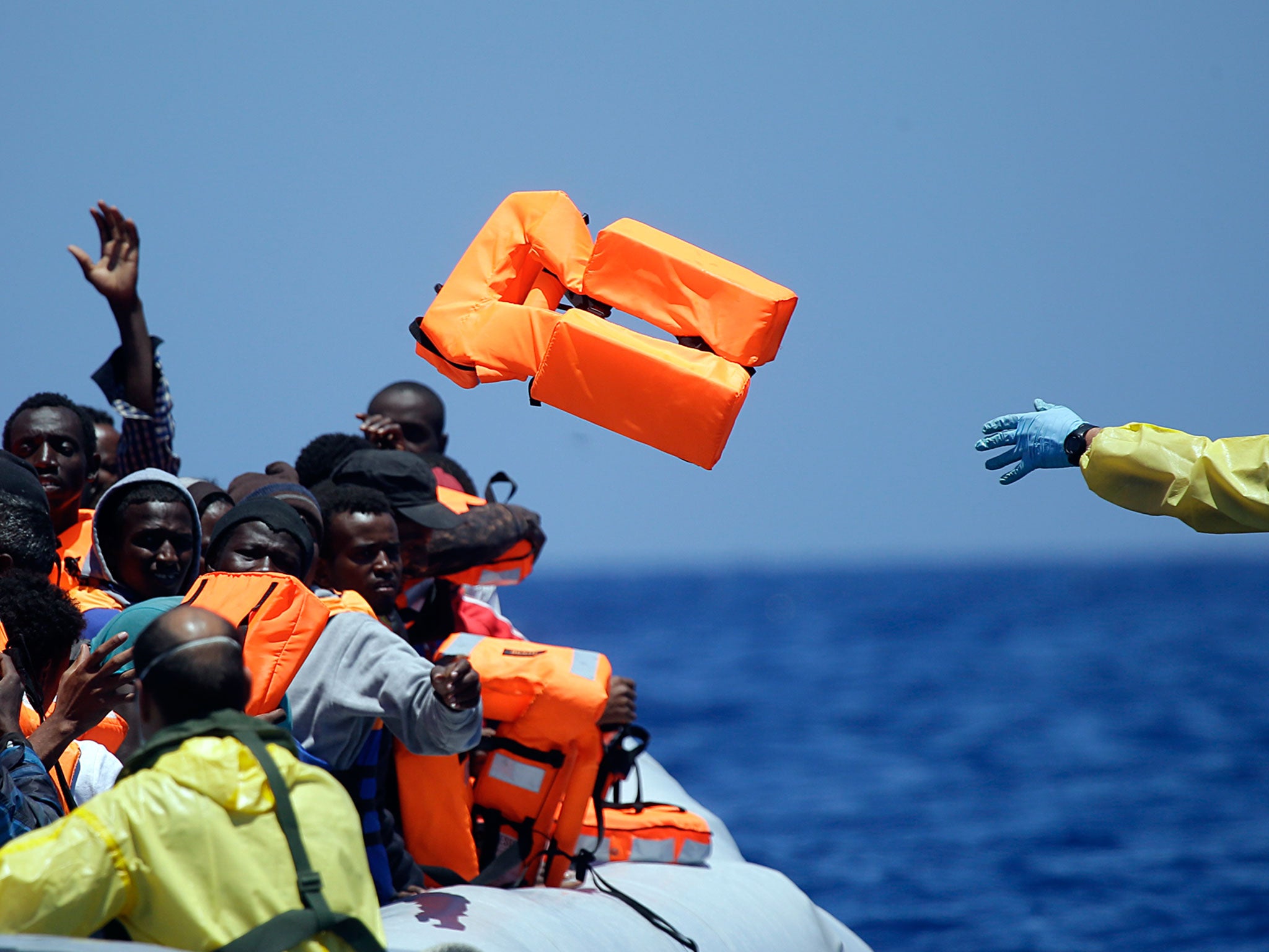 A Belgian navy sailor passes life vests to migrants sitting in a rubber boat as they approach the Belgian Navy Vessel Godetia