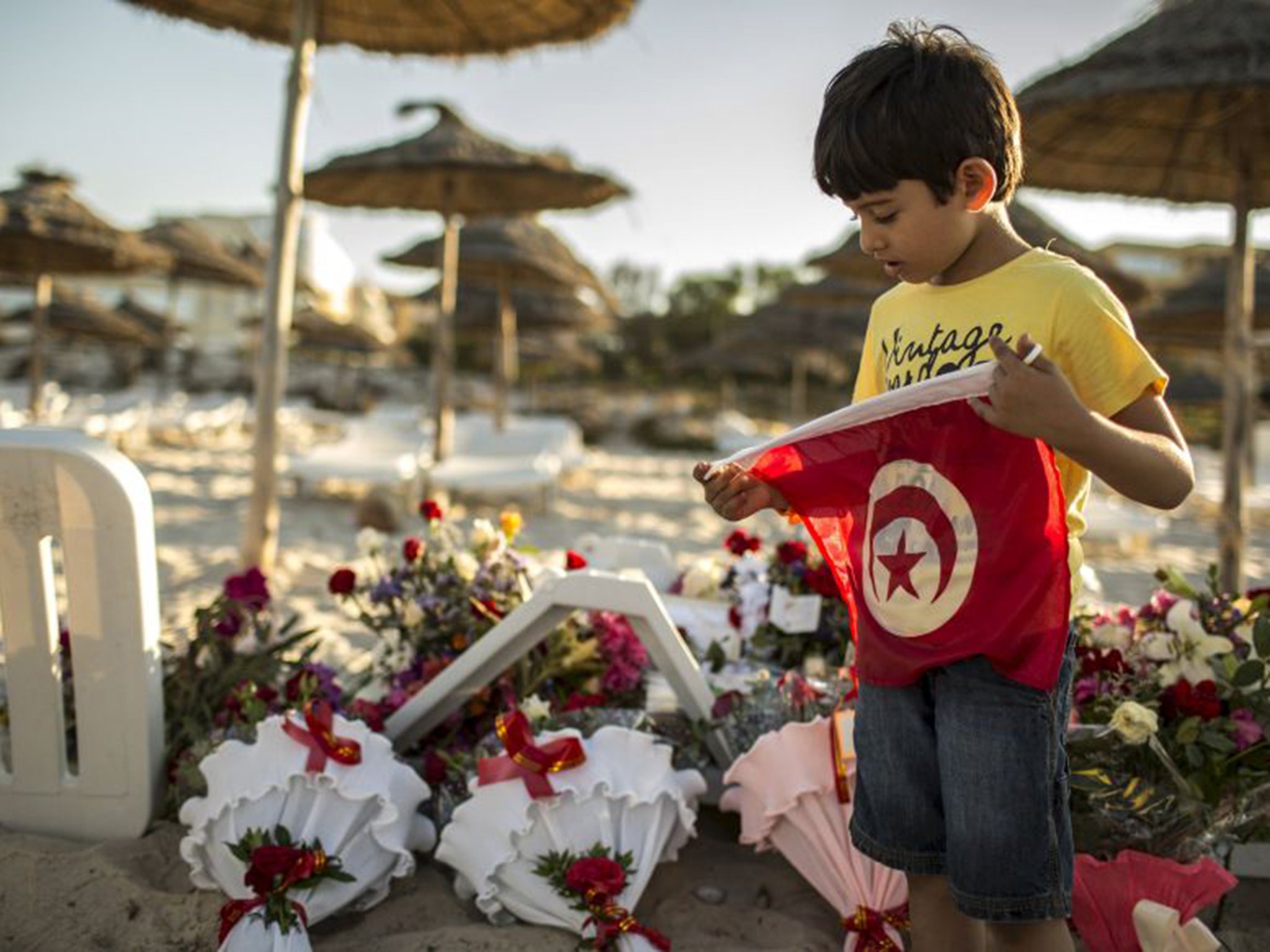 A boy holds a Tunisian flag at the spot on the beach where the attack took place