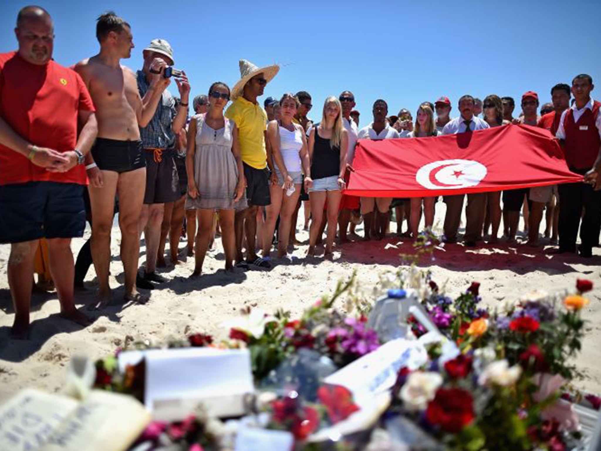 People stand in silence next to flowers during a gathering at the scene of the attack in Sousse