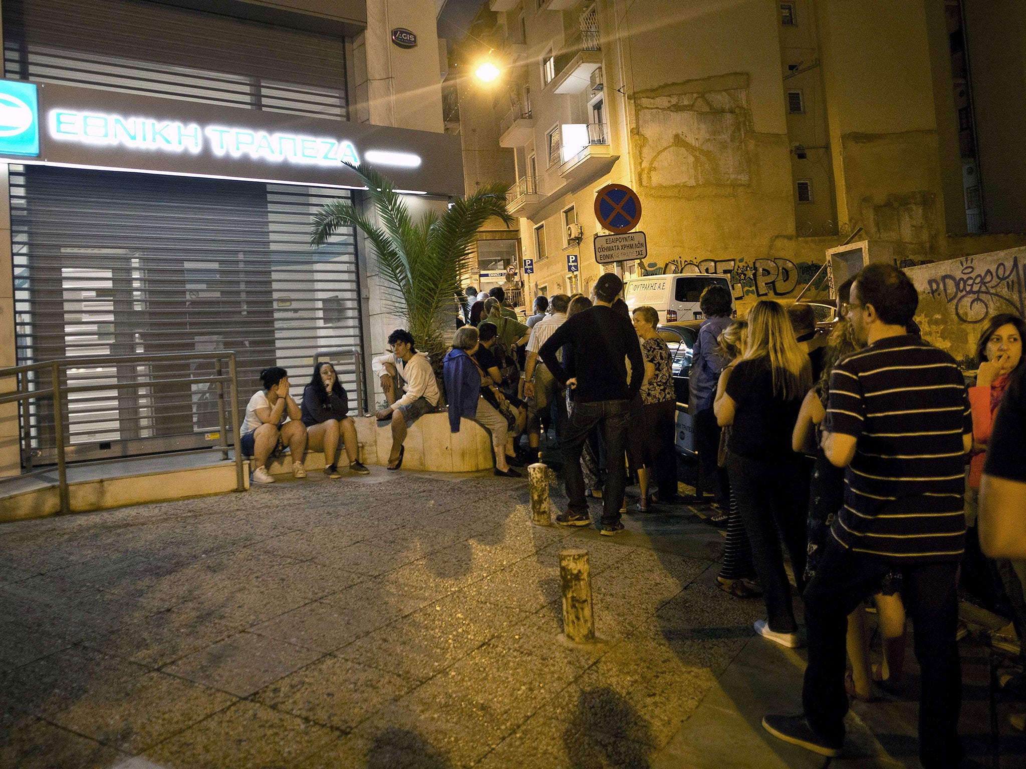 Greek people queue in front of an ATM mache to withdraw cash from a National Bank of Greece in central Athens on June 28, 2015