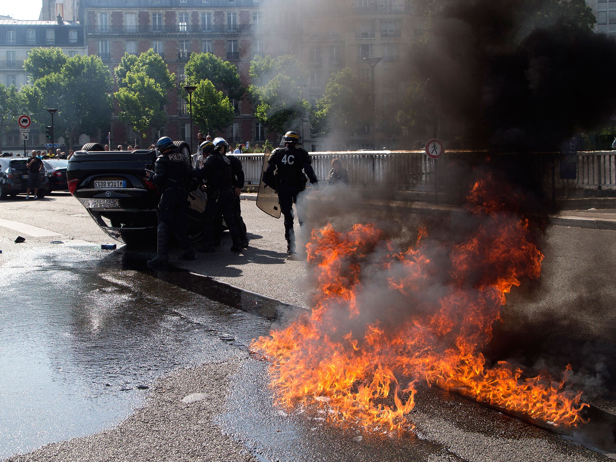 Riot police officers stand by an overthrown car during a taxi drivers demonstration in Paris, France. French authorities took two Uber managers into custody for questioning over 'illicit activity' involving its low-cost service. The detentions came amid r