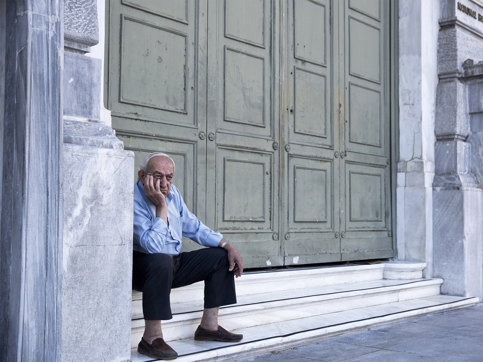 An elderly man waits to receive his pension outside the closed National Bank of Greece headquarters in Athens