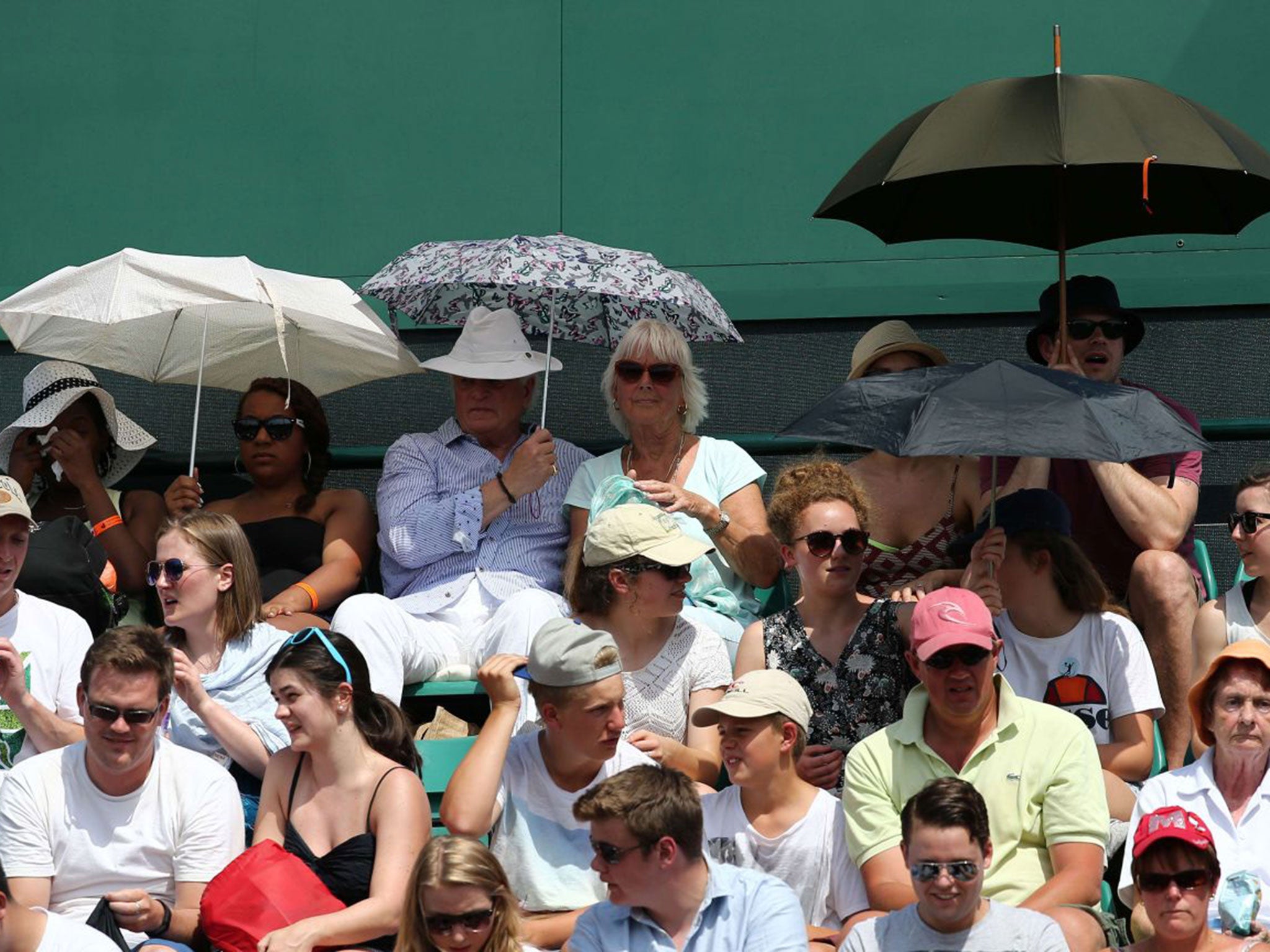 The crowds at Wimbledon seek shelter from the heat under umbrellas