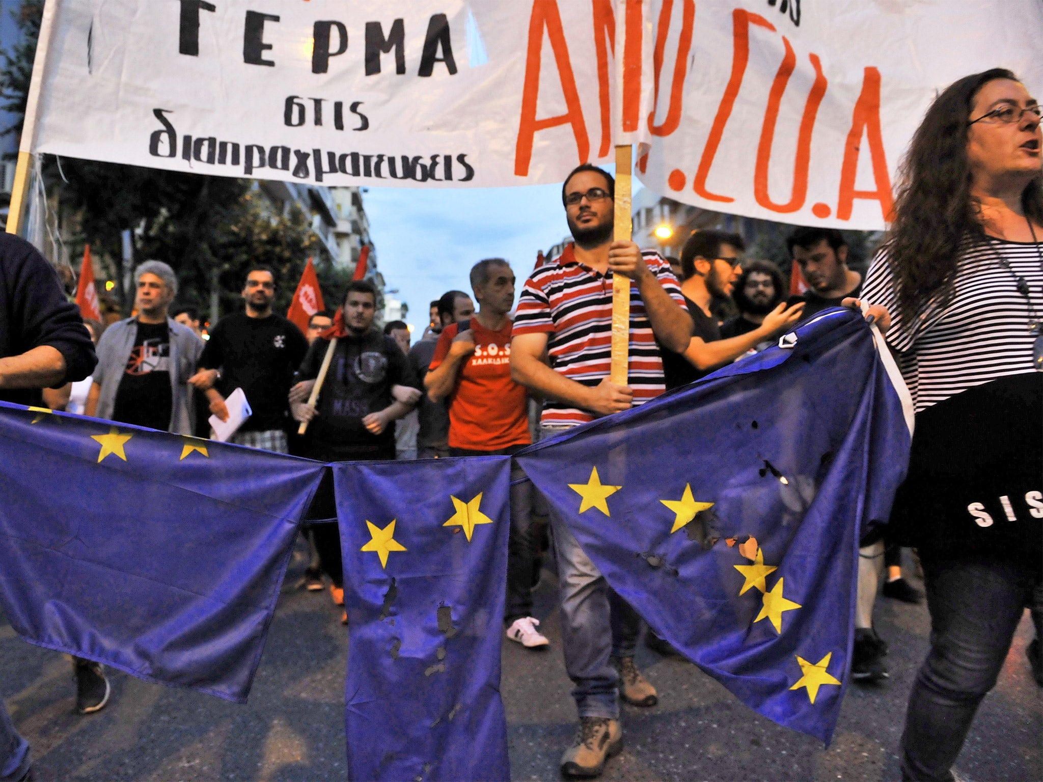 Protesters march holding a torn European Union flag during a demonstration for the 'NO' campaign in Thessaloniki