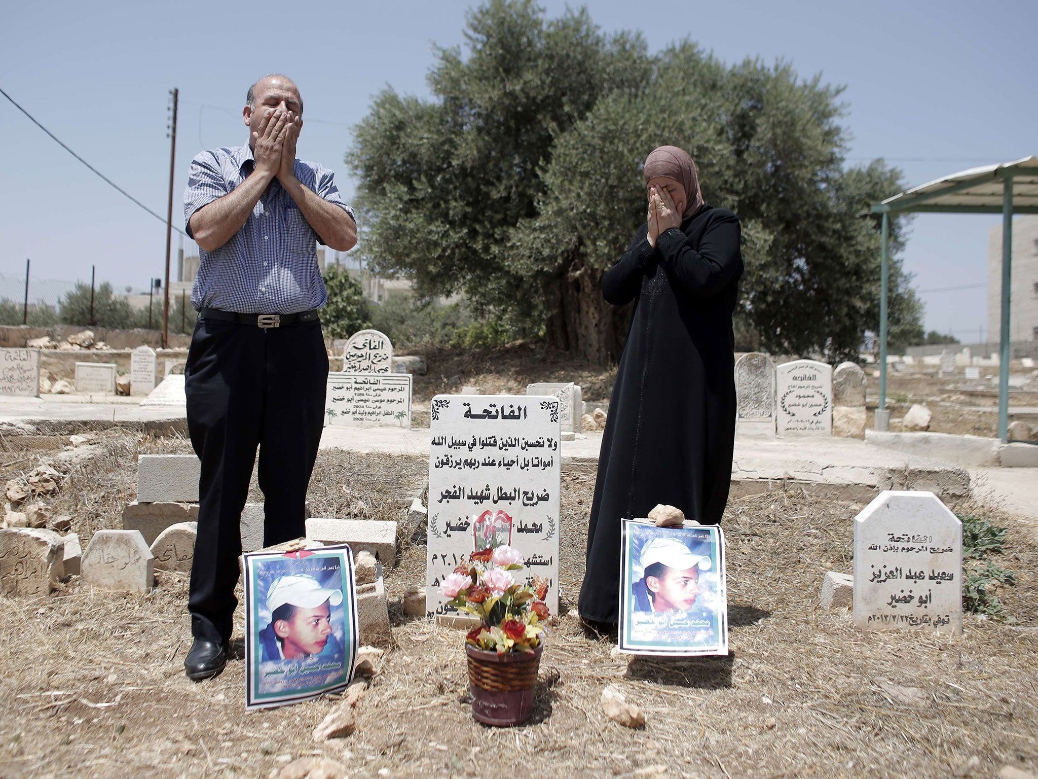 The father and mother of Palestinian teenager Mohammed Abu Khdeir pray at his grave as they mark one year anniversary since his killing by Israelis who burned him alive in revenge for the murder of three Israeli teenagers in Shuafat, in Israel's annexed East Jerusalem