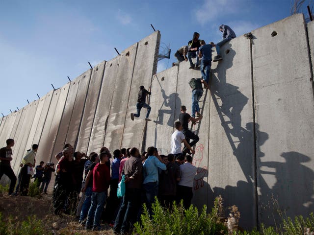Palestinians use a ladder to climb over the separation barrier with Israel on their way to pray at the Al-Aqsa Mosque on the third Friday of the Muslim holy month of Ramadan, in Al-Ram, north of Jerusalem, Friday, 26 June 2015