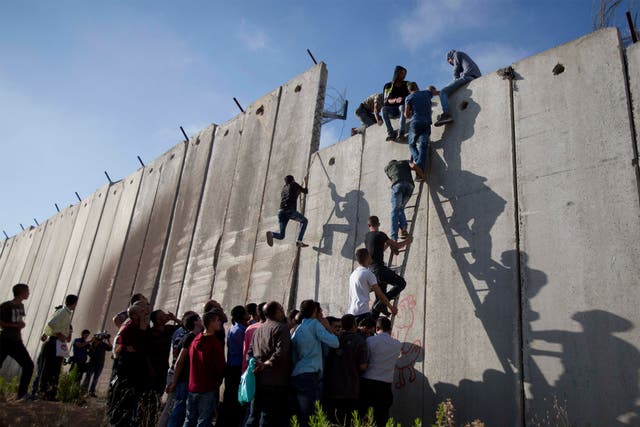 Palestinians use a ladder to climb over the separation barrier with Israel on their way to pray at the Al-Aqsa Mosque on the third Friday of the Muslim holy month of Ramadan, in Al-Ram, north of Jerusalem, Friday, 26 June 2015