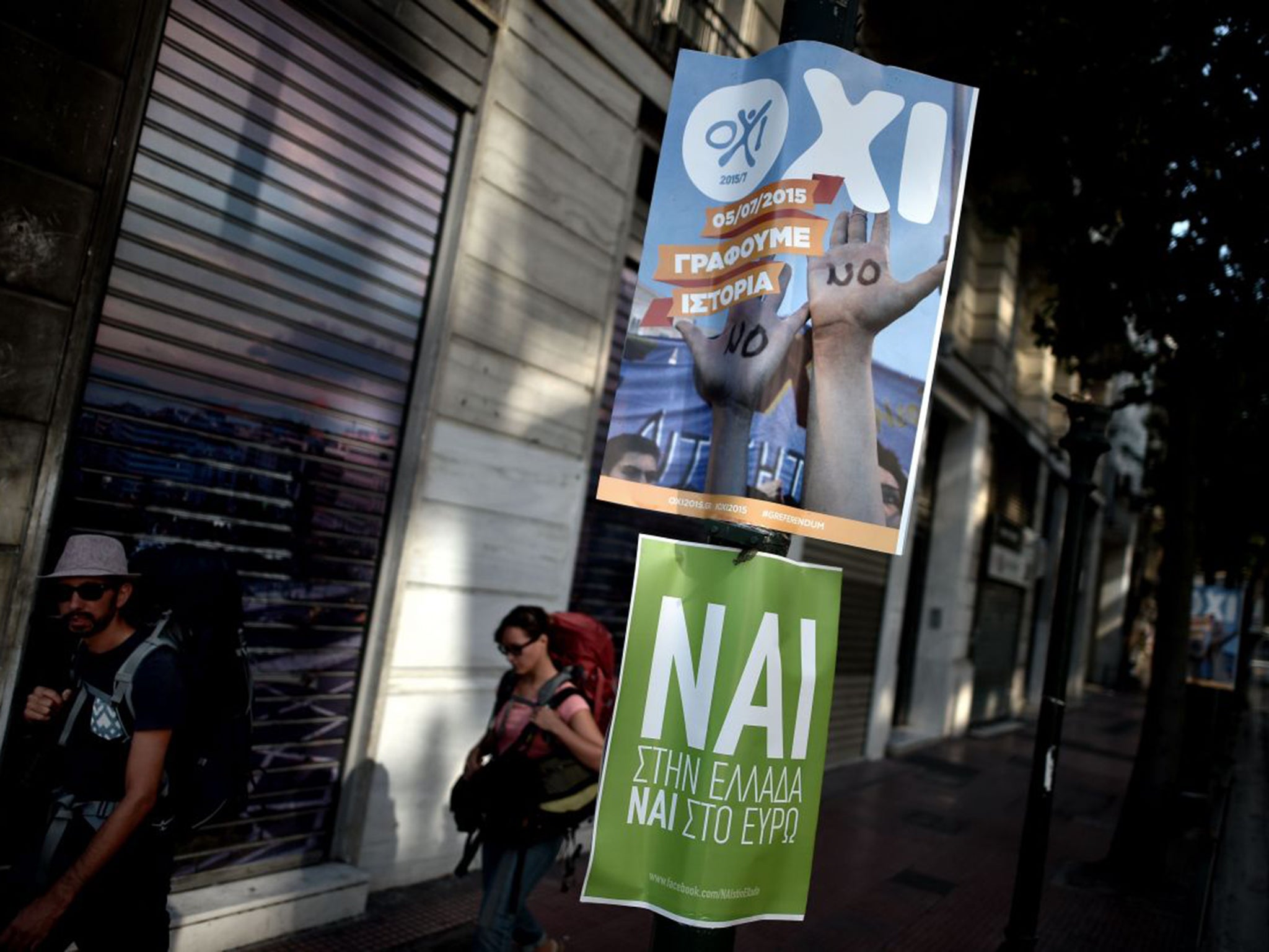 Tourists walk past posters with slogans that read “OXI“ (NO) and “NAI“ (YES) ahead of the referendum in Athens
