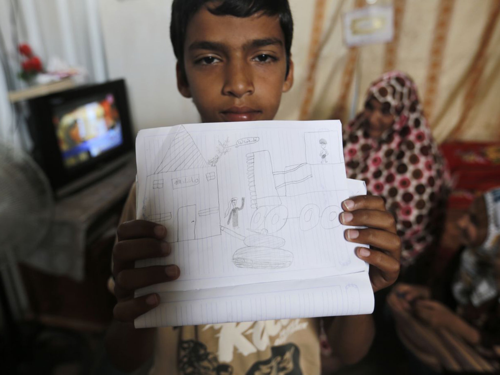 Ahmed al-Najjar, 13, shows a picture he drew of the Israeli bombs falling. He lives with his family in one of the caravans in Khuzaa