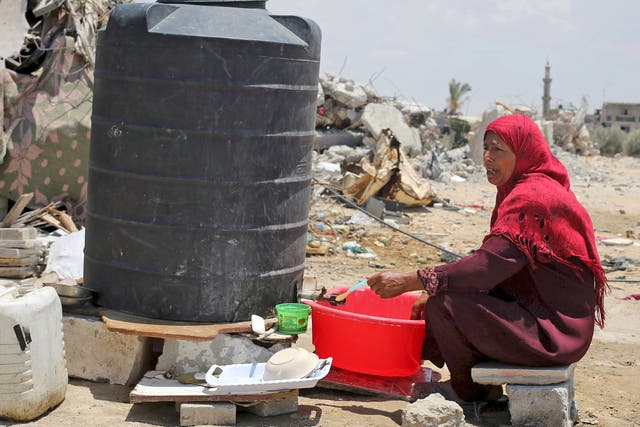 A Palestinian woman fills water from a tank near the remains of her house, in Khan Younis, Gaza