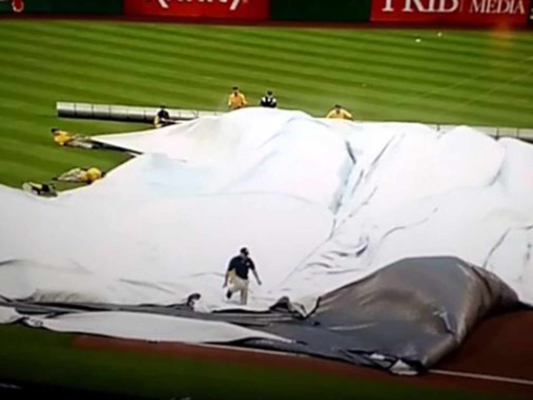 The ground staff attempt to lay down a tarpaulin sheet on the pitch