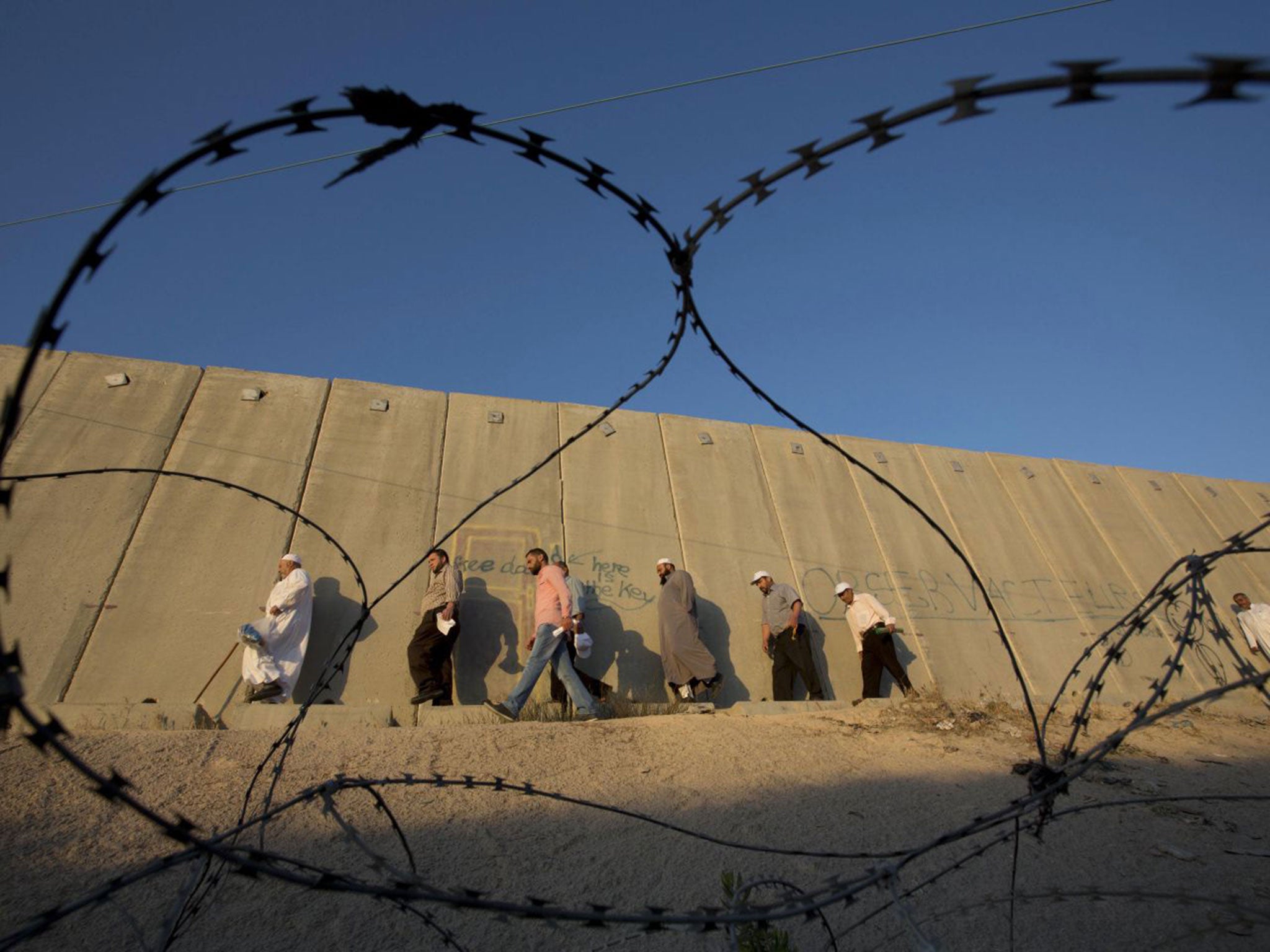 Palestinian men walk past a section of Israel's separation barrier to cross the Qalandia checkpoint on their way to pray at the Al-Aqsa Mosque in Jerusalem