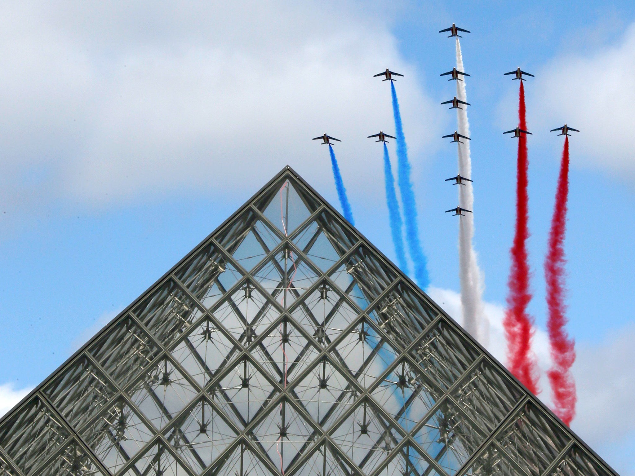 Alphajets from the French Air Force Patrouille de France in the formation of a Croix de Lorraine cross, fly over the Pyramid of the Louvre Museum