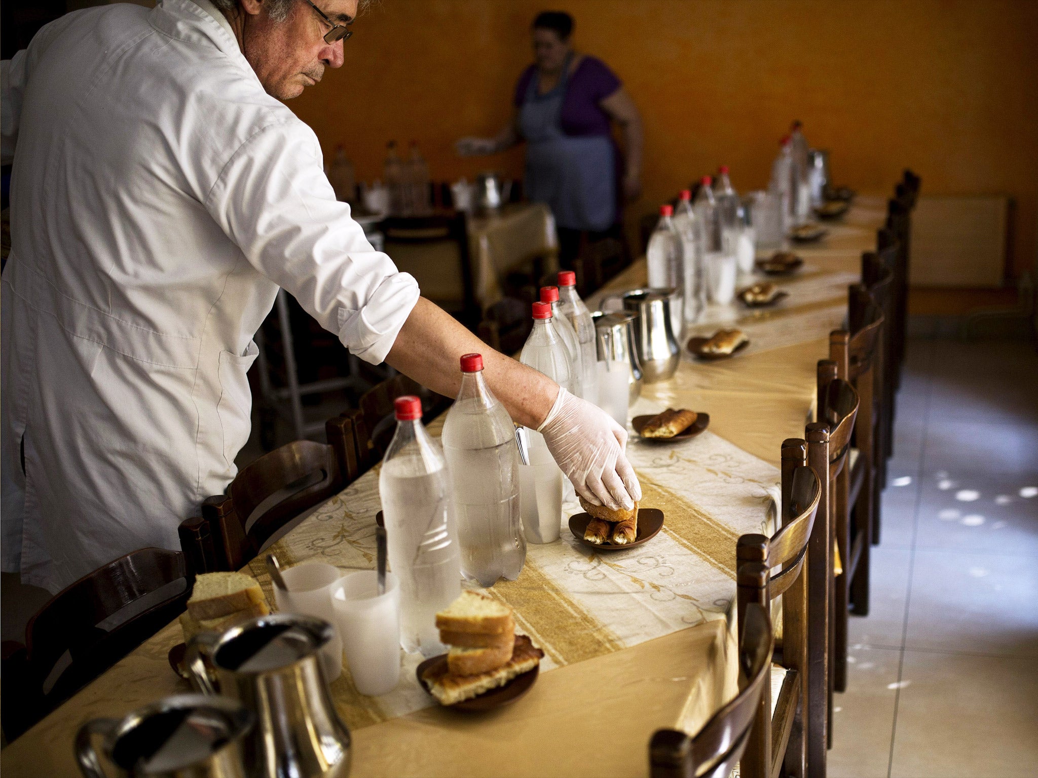 A volunteer at a Church-run soup kitchen setting the table in central Athens