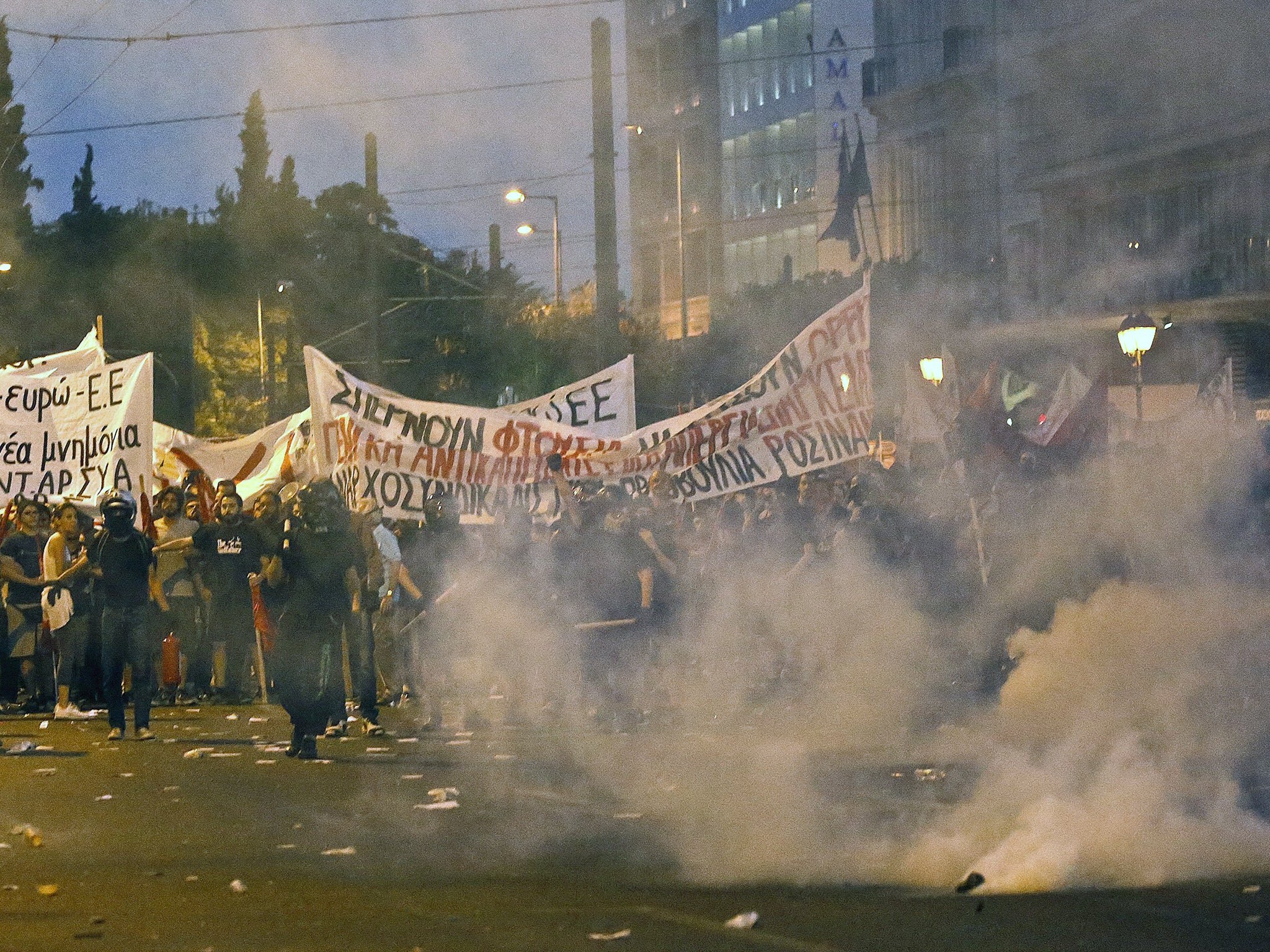 Masked anti-establishment youths and anti-austerity protesters are seen through a cloud of tear gas during clashes