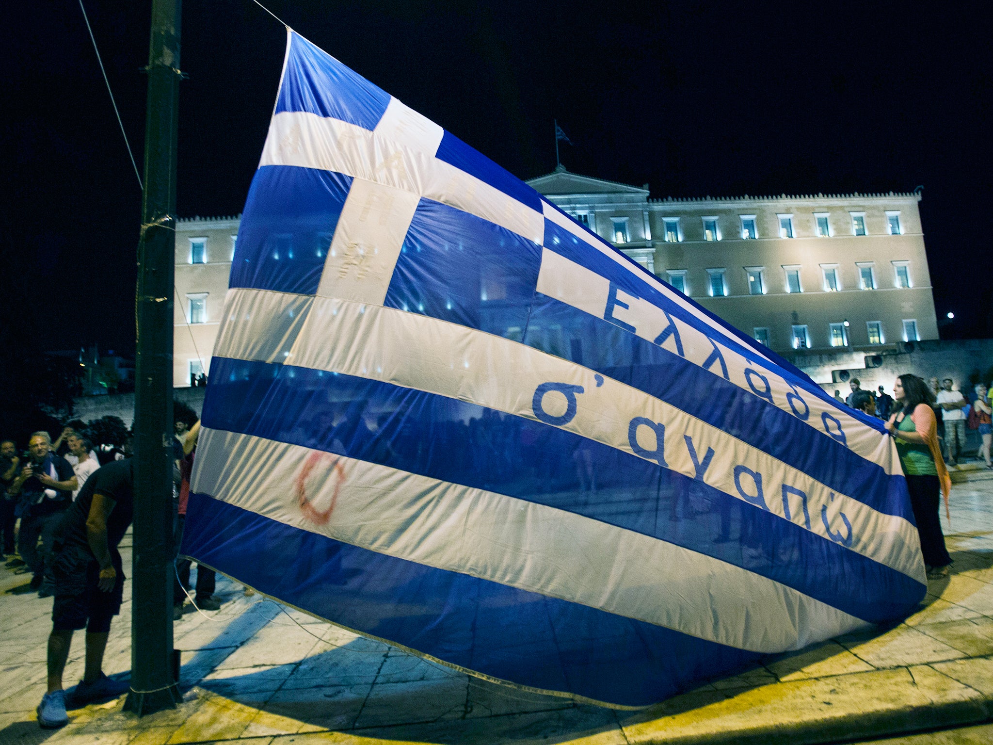 Protesters raise a Greek flag with a writing reading ''Greece we love you'' during a rally outside the Greek Parliament