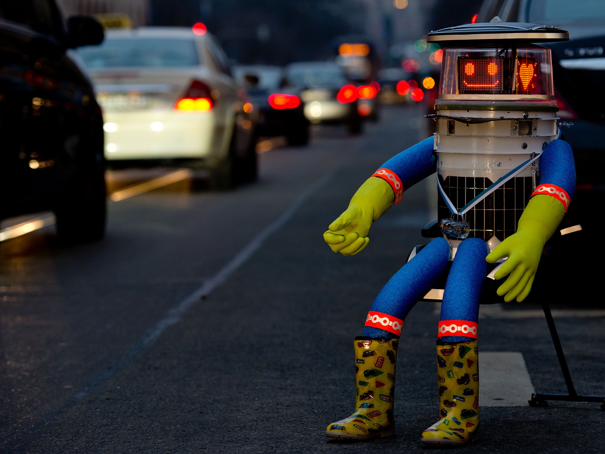 A robot called 'hitchBOT' sits on the side of a road and shows a smiling 'face' display