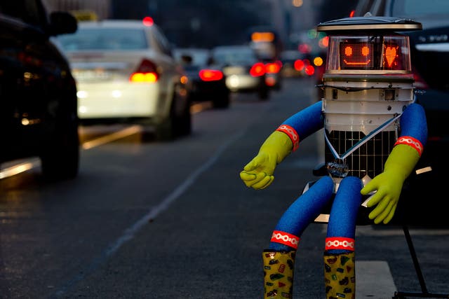  A robot called 'hitchBOT' sits on the side of a road and shows a smiling 'face' display