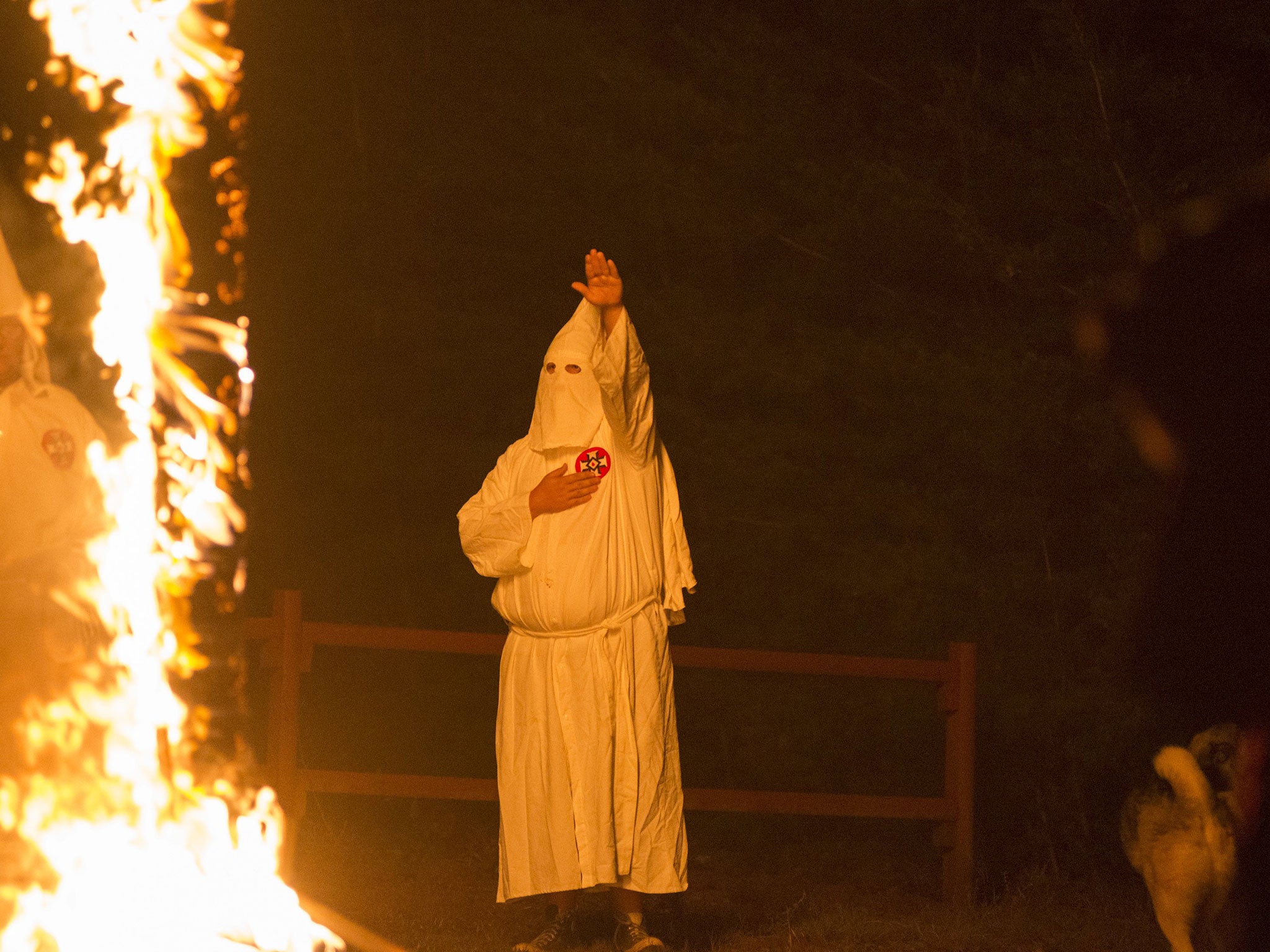 A member of the Ku Klux Klan salutes a lit cross during a cross lighting ceremony at a private residence in Henry County, Virginia,