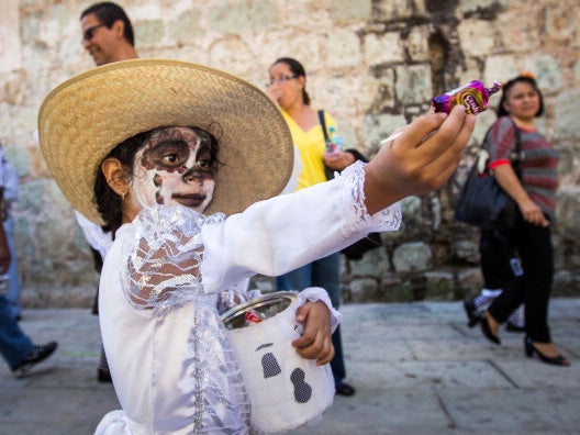 A costumed child hands out sweets during a parade through Oaxaca, Mexico during the Day of the Dead festival, used to pray for and remember family and friends who have died