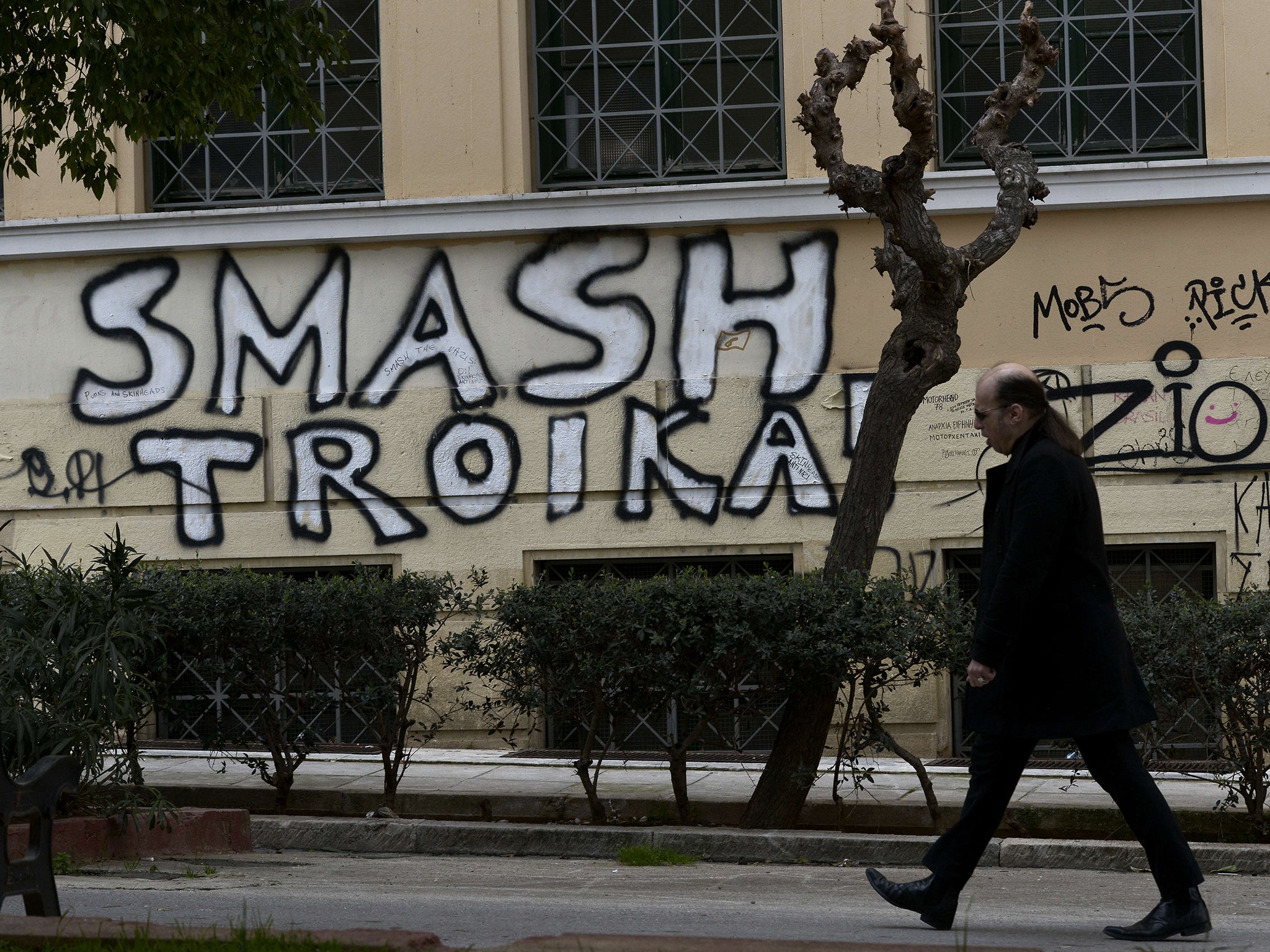 A man passes by graffiti denouncing the troika in central Athens in March