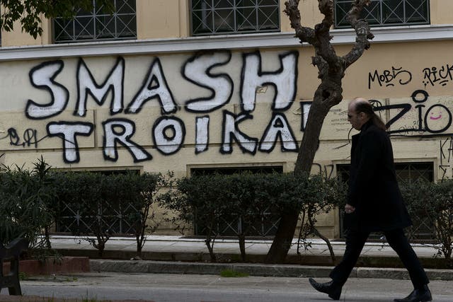 A man passes by graffiti denouncing the troika in central Athens in March