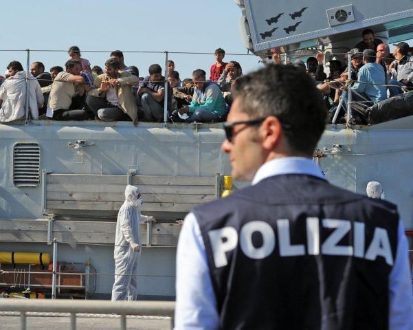 An Italian policeman stands guard as migrants wait and see if they'll be let ashore