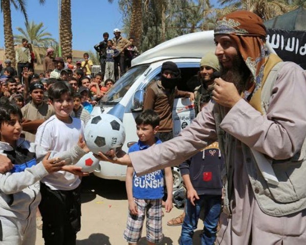 In an undated photo published by an Isis website, a jihadi fighter is see giving a boy a football during a street preaching event in Raqqa province, northern Syria