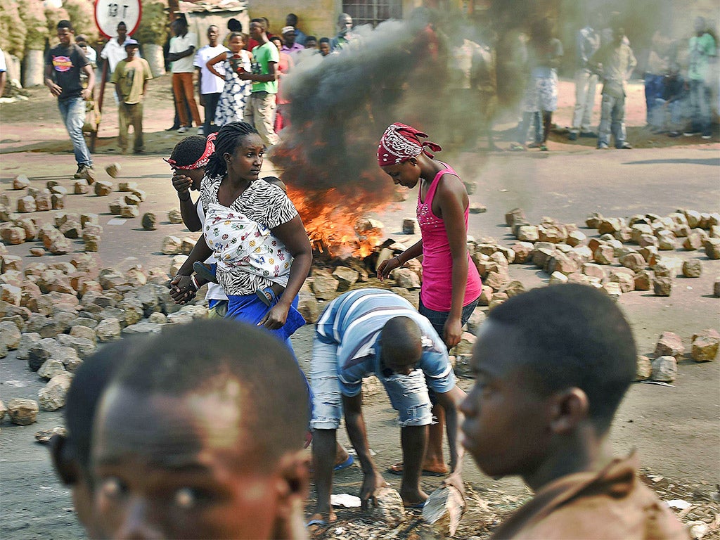 Women walk past a burning barricade set up by protesters in the Nyakabiga district of Bujumbura as violence rocked the capital during voting