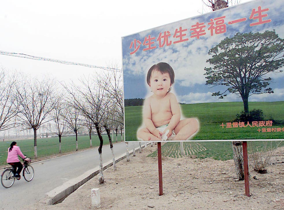 A woman cycles past a poster reminding citizens of China's one-child policy