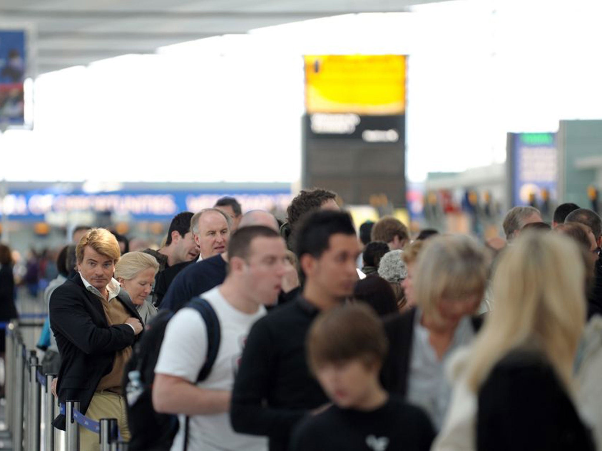 Airline passengers queue for the Check-In counters while awaiting information about flight cancellations in Terminal 5