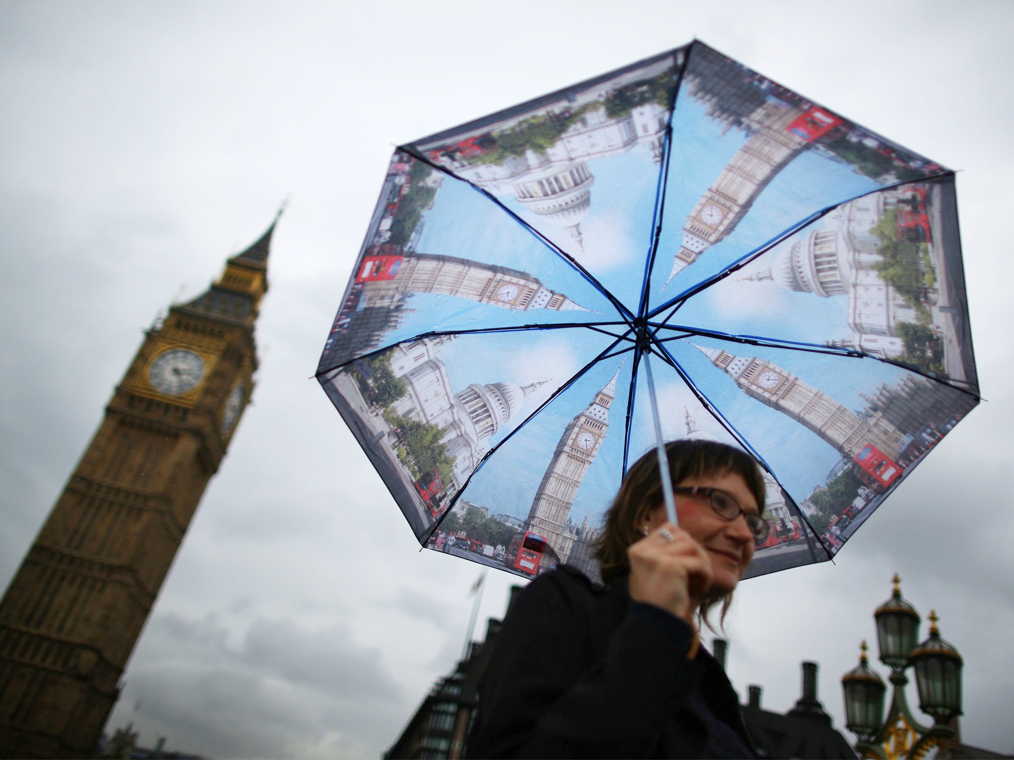 A visitor shelters from the rain under an umbrella decorated with images of Big Ben and St Paul's as she walks near Parliament in London. Downpours are being experienced in parts of the United Kingdom