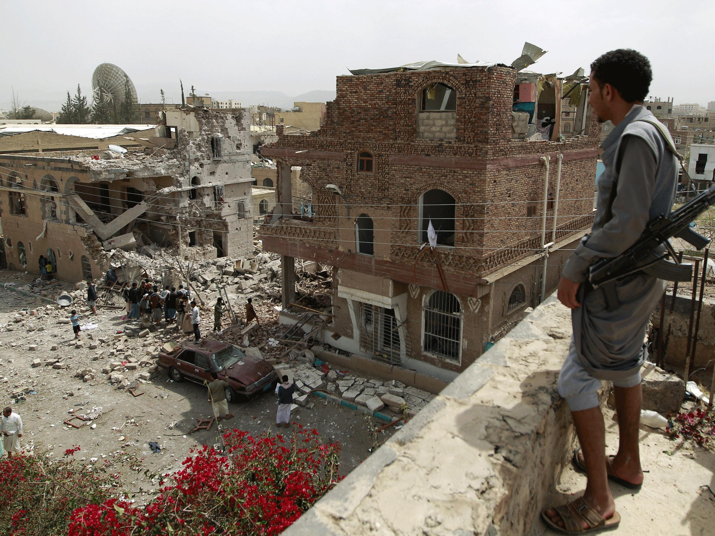 A Huthi militant watches from the roof of a building as people inspect the debris of a house destroyed in an air-strike by the Saudi-led coalition on the capital of Sanaa