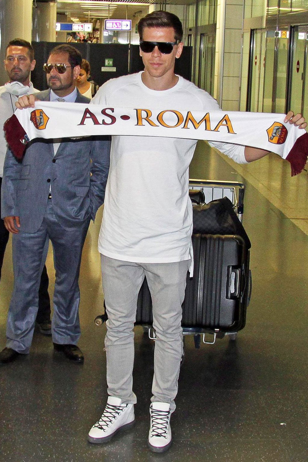 Szczesny holds a Roma scarf as he leaves the airport in Roma