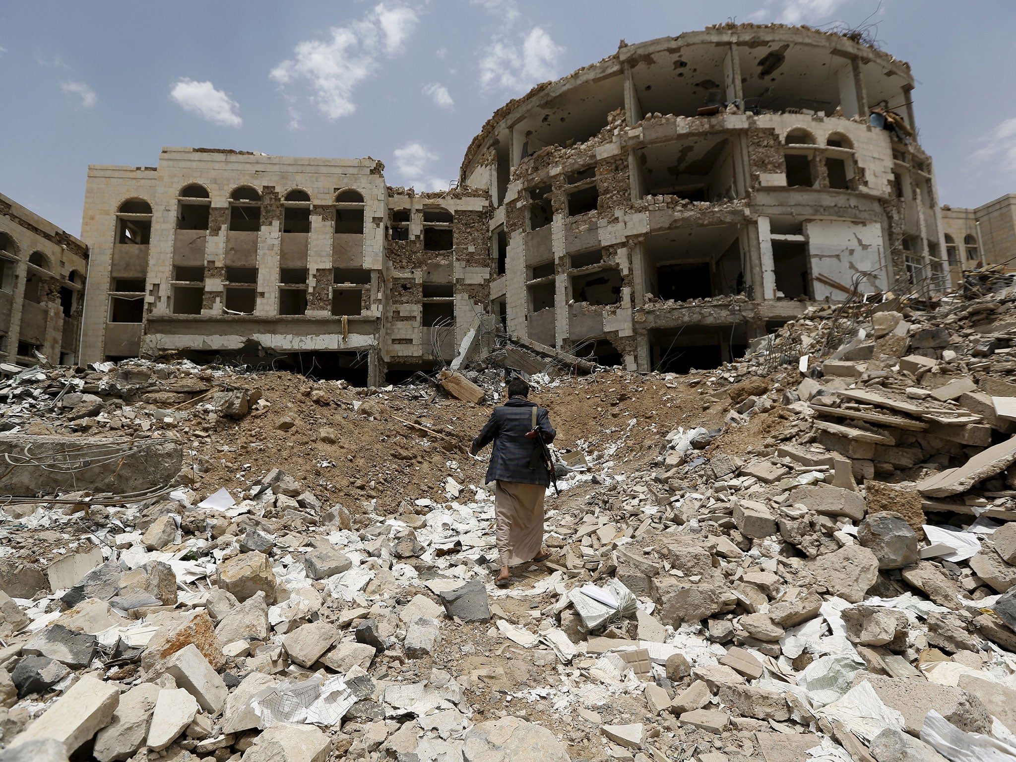 A Houthi militant walks in front of a government compound, destroyed by recent Saudi-led air strikes, in Yemen's northwestern city of Amran
