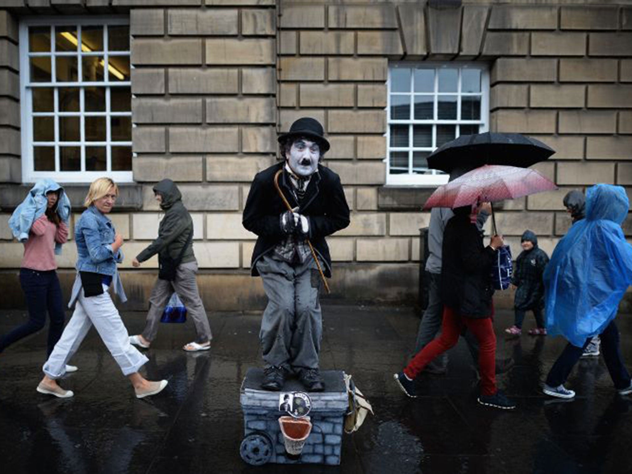 Members of the public, walk past a street entertainer on the Royal Mile